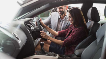 A young lady sits behind the wheel of her car reviewing the dashboard.